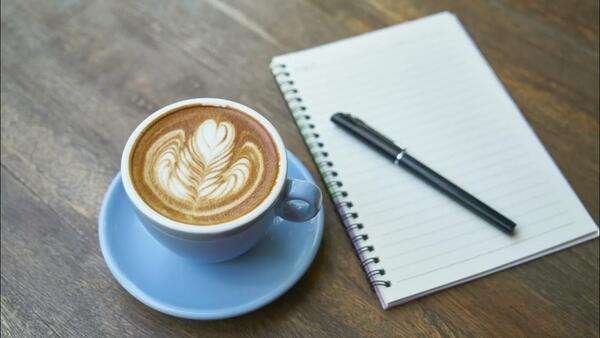 Puodelis ant stalo šalia užrašų knygelės ir švelnios šviesos